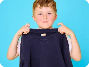 garçon tenant un pull bleu avec une etiquette vetement bebe