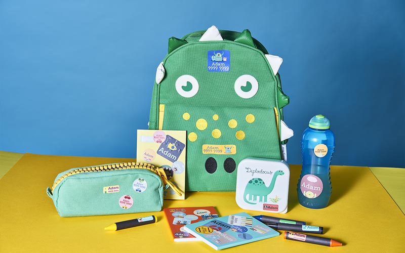 grands autocollants nominatifs et petits autocollants nominatifs de My Nametags sur des livres, des crayons et des sacs sur fond jaune
