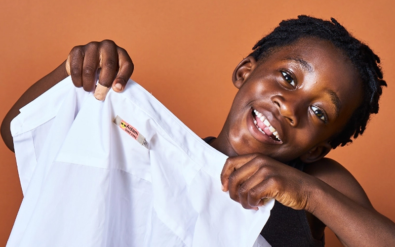 Enfant tenant une chemise avec une étiquette thermocollante My Nametags attachée, sur fond marron